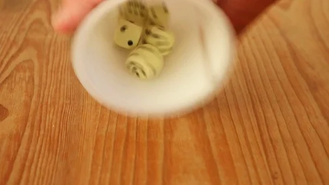Mixing up five dice in a cup and shaking them out on to the table. Stock Footage 93462412
