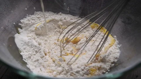 Mixing flour eggs and milk with eggbeater in a glass bowl slow motion Stock Footage 169237963