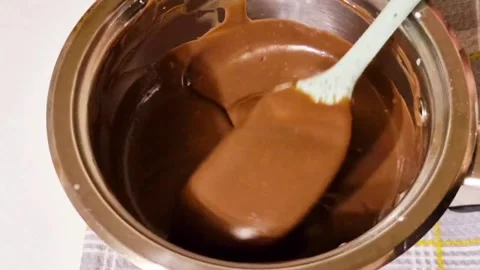 Mixing smooth melted dark chocolate in a stainless steel bowl with a spatula Stock Footage 326633649