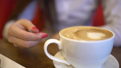 Mixing sugars into a cup of latte coffee, slow motion. Close-up of the woman's Stock Footage 85364891