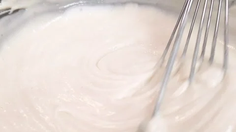 Mixing thick, white, creamy batter with a metal whisk in a bowl during the Stock Footage 343879366