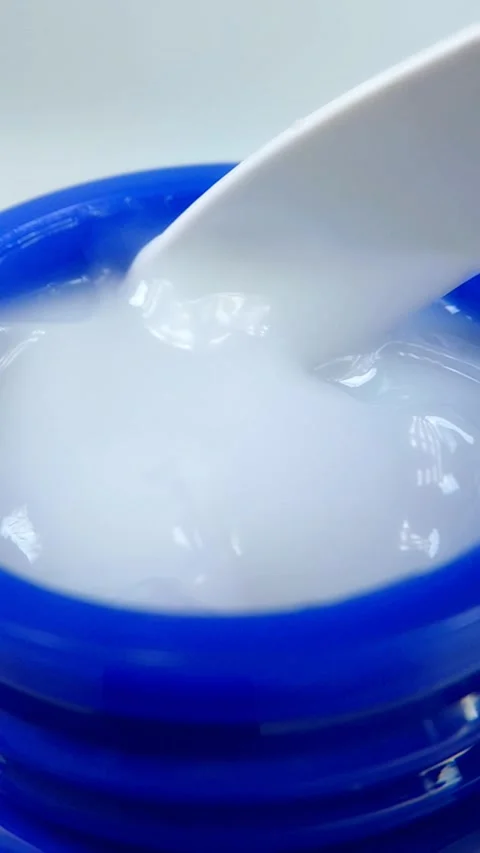 Mixing white moisturizing cream in blue tube with plastic spoon, Stock Footage 335296829