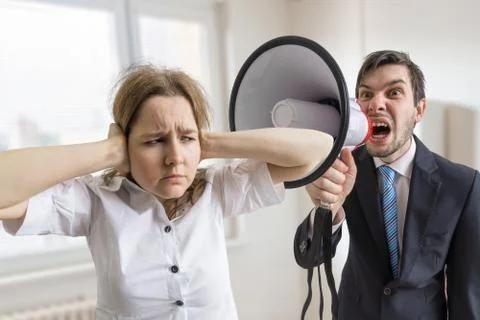 Mobbing at work. Manager is shouting at his secretary at work with megaphone. Stock Photos
