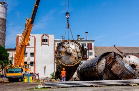 Mobile crane lay down big old metal tank Worker is helping to keep balance an Stock Photos