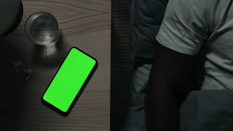 Mobile with green screen on table while man falling asleep 動画素材 163706503
