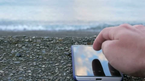 The mobile phone is about the pebble beach of the ocean. Man looking for your Stock Footage 67616435