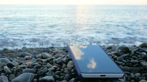 The mobile phone is about the pebble beach of the ocean. Calm waves beating Stock Footage 67618182