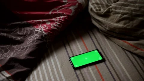 A mobile phone appears from under the covers on the bed. Stock Footage 147227599