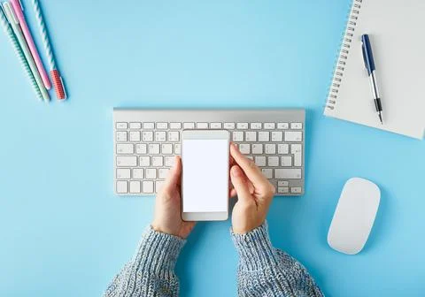 Mobile phone with blank white screen display in hand. Bright blue modern desk Stock Photos
