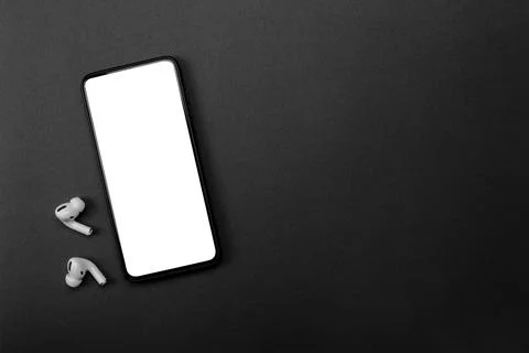 Mobile phone with empty screen and earphones on black surface. Wireless earph Stock Photos