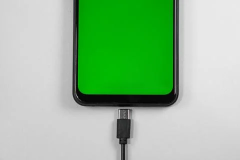 Mobile phone with green screen connected to a charger on white background Stock Photos
