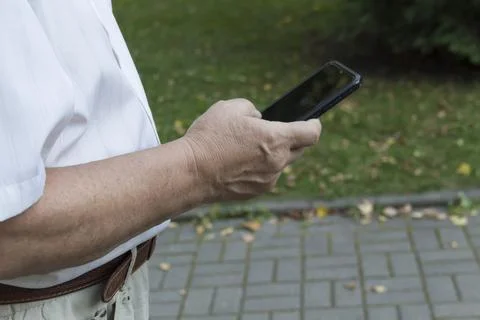 A mobile phone in the large hands of an elderly man in a white shirt on a walk Stock Photos