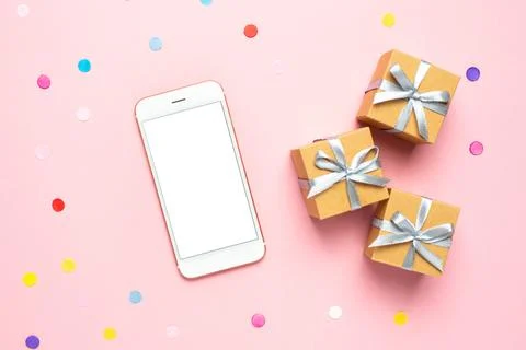 Mobile phone, present boxes and color confetti on pink table. Composition f.. Stock Photos