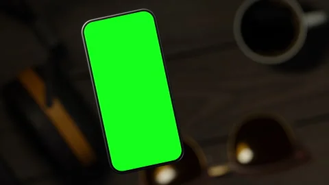The mobile phone is slightly raised above the wooden table, showing the scree Stock-Footage 261365664