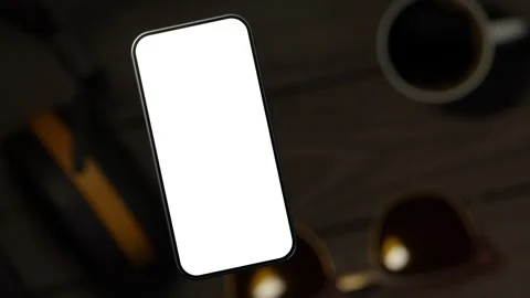The mobile phone is slightly raised above the wooden table, showing the scree Stock-Footage 261365689