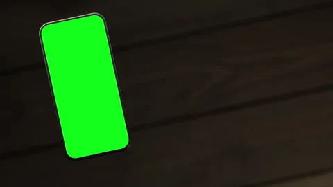 The mobile phone is slightly raised above the wooden table, showing a green s Stock Footage 261365814