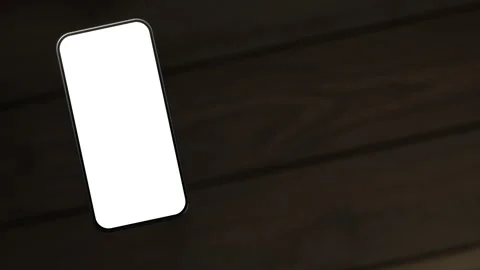 The mobile phone is slightly raised above the wooden table, showing a white s Stock Footage 261365822