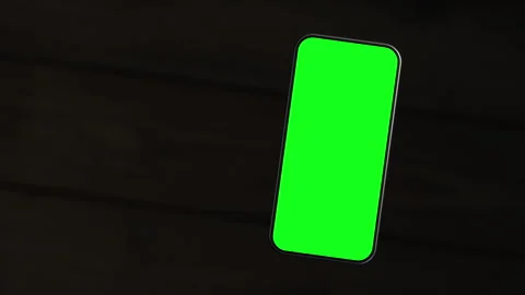 The mobile phone is slightly raised above the wooden table, showing a green s Stock-Footage 261365852