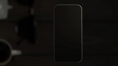 The mobile phone is slightly raised above the wooden table, showing the scree Stock-Footage 261365924