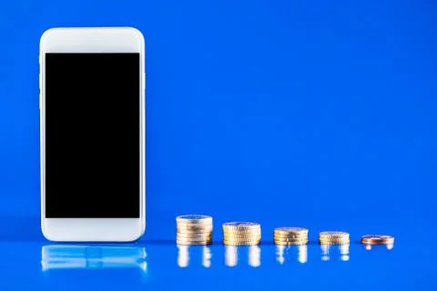 Mobile phone with stack of coins on blue background. Business growth and fina Stock Photos