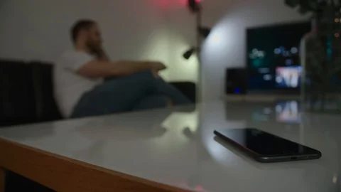 Mobile phone on a table, man watching tv in the background. Stock Footage 120876047