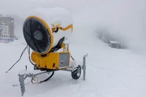A mobile snow making machine on ski slope pumps out snow. Stock Photos