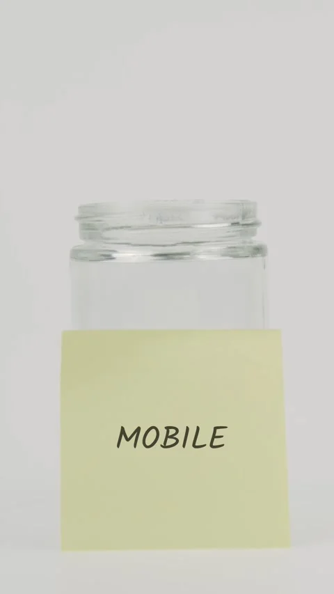 Mobile text or word on yellow sticky note attached to glass jar with hand 스톡 동영상 311756001