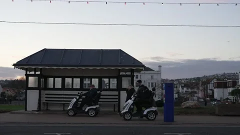 Mobility scooter OAP roll past parking meter and victorian beach front shelter Vídeo Stock 224731003