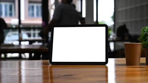 Mock up digital tablet with blank screen and coffee cup on wooden table. Stock Photos
