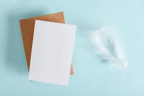 A mock-up of an envelope, a white sheet of paper and white feathers on a ligh Foto stock