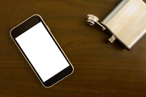 Mock up flat lay of blank smartphone screen and open empty flask on the table 库存照片