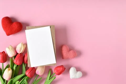 A mock-up of a kraft envelope with a blank sheet, tulips and knitted hearts. Stock Photos