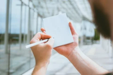 Mock Up notebook in a man's hand, against the background of a glass building. Stock Photos