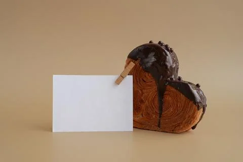 Mock up template paper note card Heart shaped dark chocolate croissant on beige Stock Photos