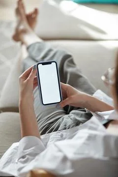 Mock up white screen blank mobile phone in woman hands holding lying on the sofa Stock-Fotos
