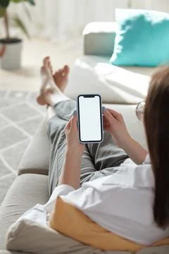 Mock up white screen blank mobile phone in woman hands holding lying on the sofa Stock Photos