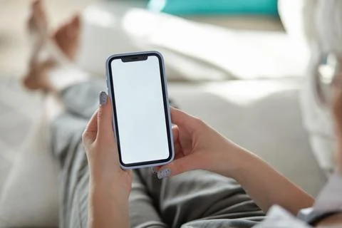 Mock up white screen blank mobile phone in woman hands holding lying on the sofa Stock Photos