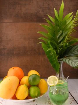 Mocktail, oranges, lemons, limes, mango, vase with leaves on brown textured Stock Photos