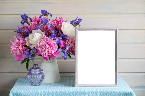 Mockup of an empty frame and bouquet of peonies and irises on a table in th.. Stock Photos