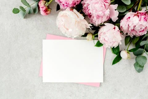 Mockup invitation, blank paper greeting card, pink envelope and peonies on gray Stock Photos