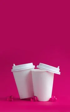 Mockup of two white coffee cups on a pink background with glass hearts. Stock Photos