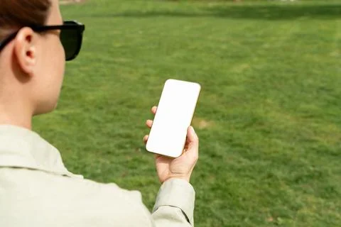 Mockup white blank screen of mobile phone in woman's hands on background of g Stock Photos