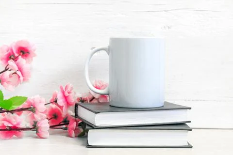 Mockup of a white ceramic mug on a table with books and flowers Stock Photos