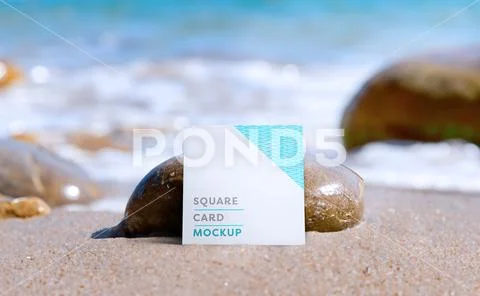 Mockup of a white square card at the edge of the beach leaning against a rock Modello PSD