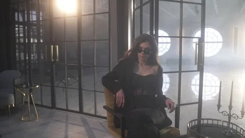 A model in the backlight of huge windows moves languidly in a chair Vidéo 261560293