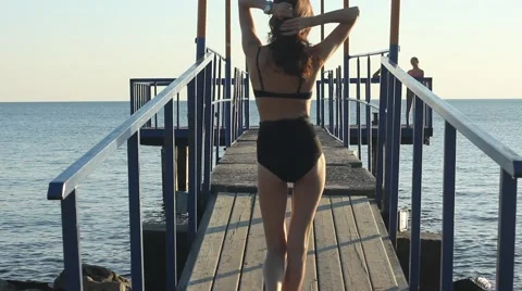 Model in black bikini catwalks runway at the  sea pier at sunset. Stock Footage 65775797