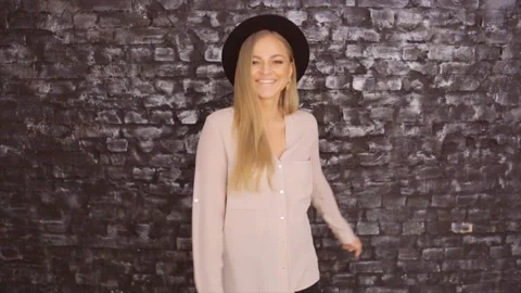 Model in a black hat and a gray shirt posing against a brick wall background Stock Footage 87323948