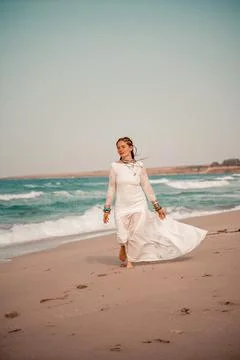 Model in boho style in a white long dress and silver jewelry on the beach. Her Stock Photos