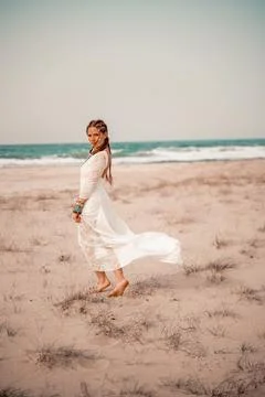 Model in boho style in a white long dress and silver jewelry on the beach. Her Stock Photos