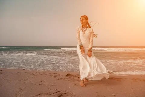 Model in boho style in a white long dress and silver jewelry on the beach. Her Stock Photos